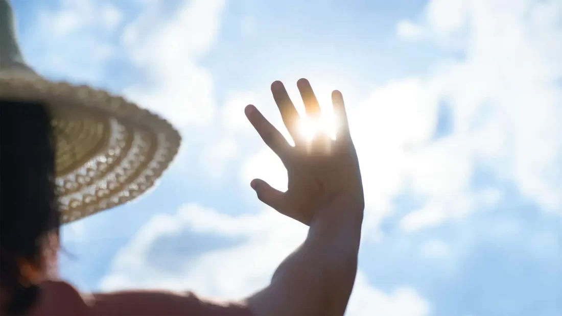 Persoon houdt hand omhoog tegen de zon tijdens een warme dag.