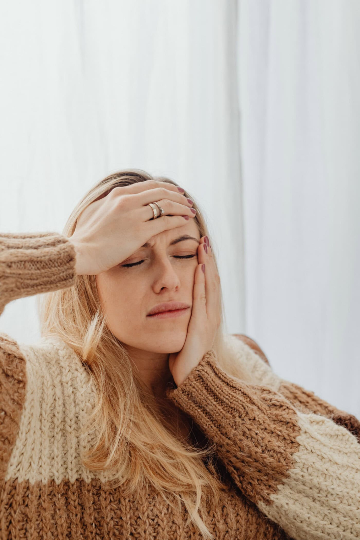 Vrouw met hoofdpijn houdt haar hoofd vast in een lichte kamer.
